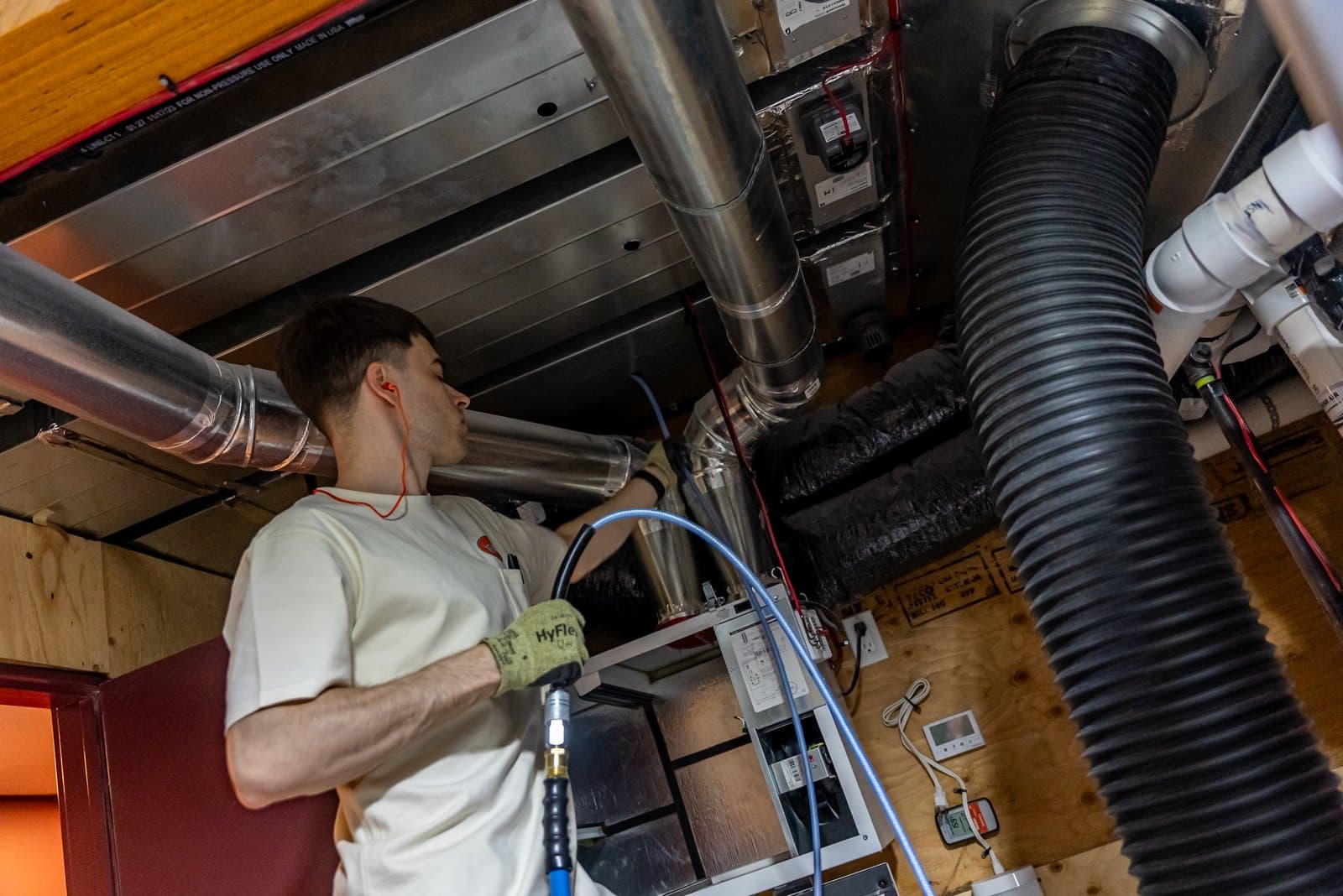 The Vent Men technician cleaning residential ducts in a Calgary basement, connected to truck-mounted equipment